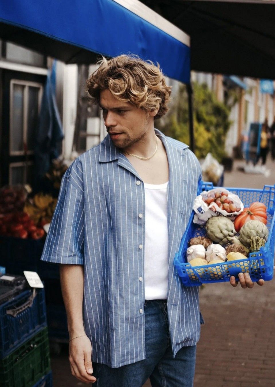 Daan van der Lecq op de markt met een blauw krat vol groente en fruit: artisjokken, tomaat, knoflook en druiven.