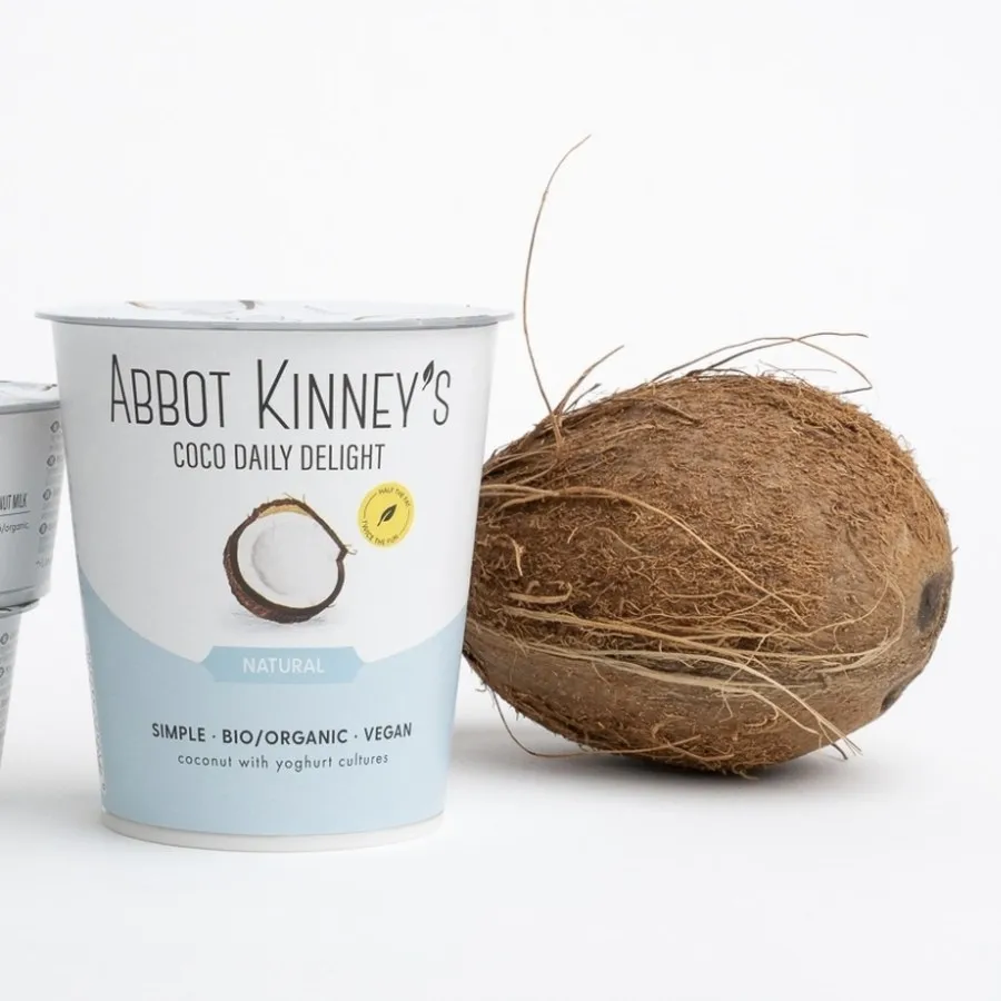 Beker Coco Daily Delight van Abbot Kinney’s naast een kokosnoot.