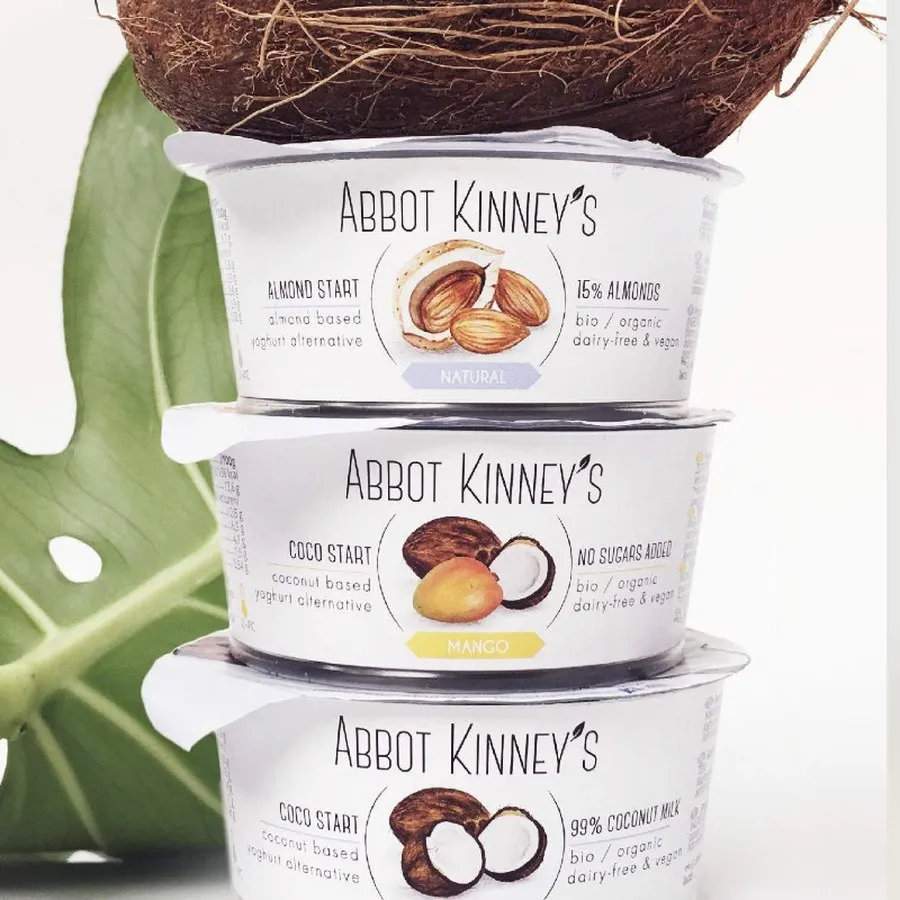 Drie bekers Abbot Kinney’s: Almond Start naturel, Coco Start mango en Coco Start naturel, met een kokosnoot erbovenop.